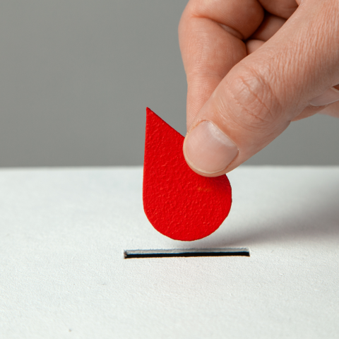 Red paper blood drop shape dropped into coin bank slot